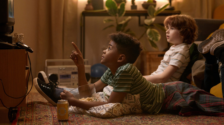 Two kids snacking in front of a T.V. in dated setting