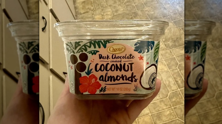 Person holding container of Choceur Dark Chocolate Covered Coconut Almonds