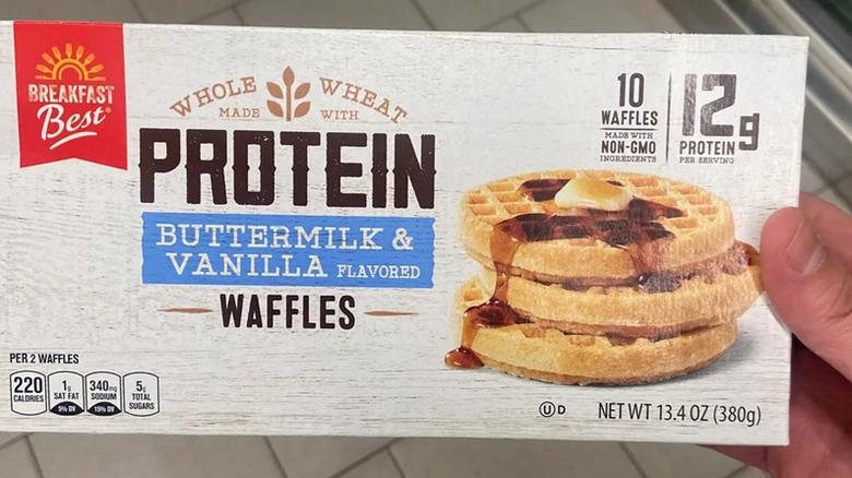 A hand holds up a package of Breakfast Best Protein Buttermilk & Vanilla Flavored Waffles