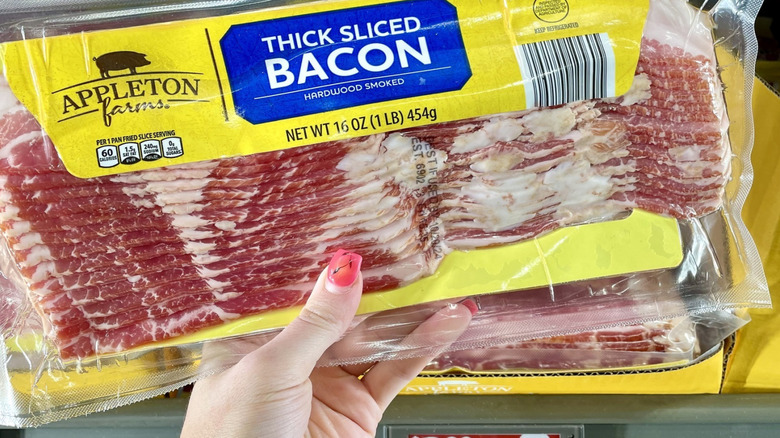 A hand holds up a package of Appleton Farms Thick Cut Bacon from Aldi