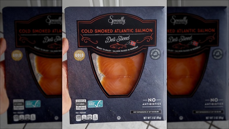 A hand holds up a package of Aldi deli-sliced salmon