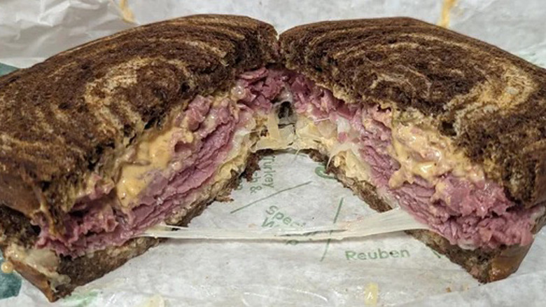 An Arby's reuben sandwich sits on a paper wrapper, cut in half and opened to show inside
