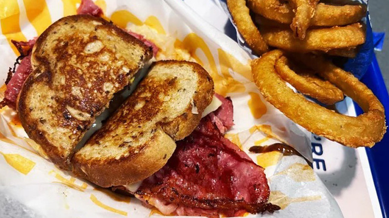 Culver's Reuben sandwich, cut in half, sits on a paper-lined plate with onion rings.