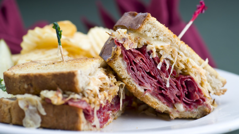 A classic reuben sandwich on rye sits on a plate with potato chips.