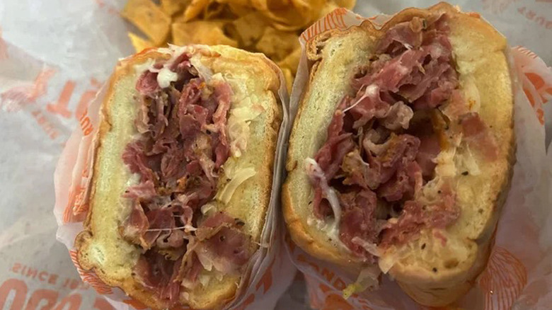 Two halves of a TOGO'S Reuben sit face up on a paper wrapper with corn chips on the side.