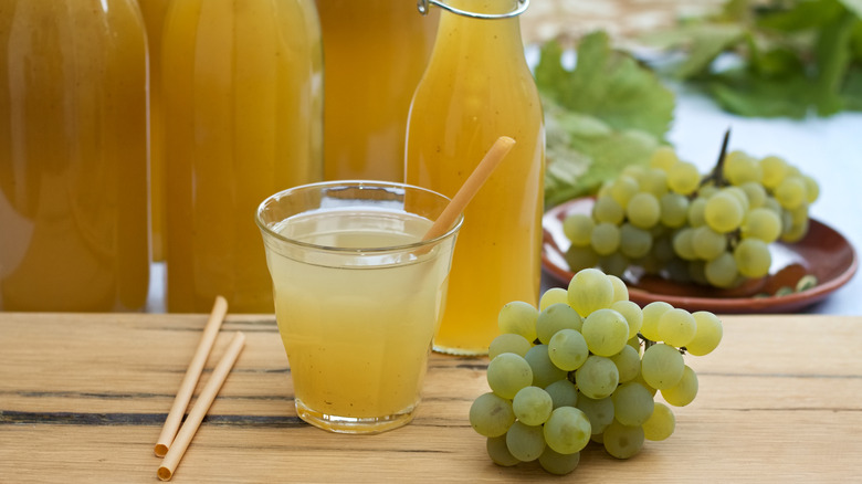 Glass of white grape juice with bunches of fresh grapes