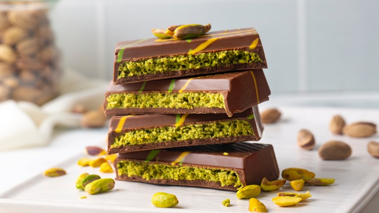 Stacked pieces of Dubai chocolate surrounded by pistachios and shells on a white plate