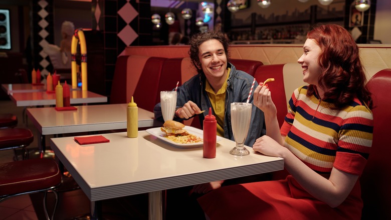 Young couple enjoying fries with a burger and milkshakes in a retro diner