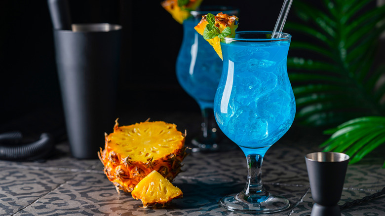bright blue drink in a glass with ice and pineapple