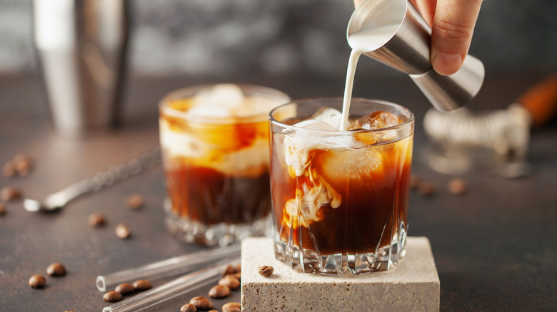 cream being added to a brown cocktail with ice