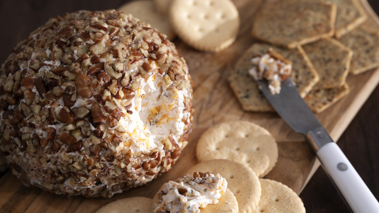 A classic cheese ball and crackers are laid out on a wooden serving board