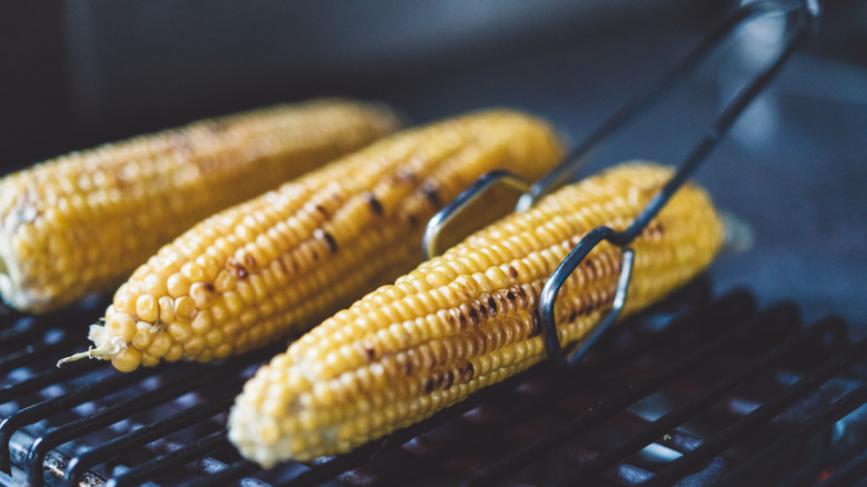 Several pieces of corn on the cob are lined on a grill with one being turned by tongs