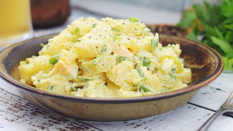 A plate of potato salad sits on a wooden table outdoors