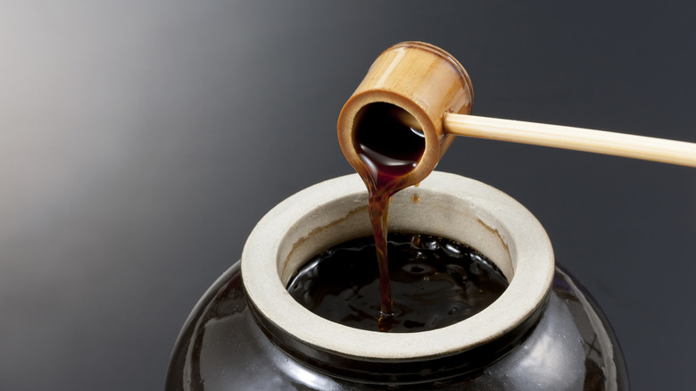 Small wooden scoop extracting black vinegar form a large ceramic jug