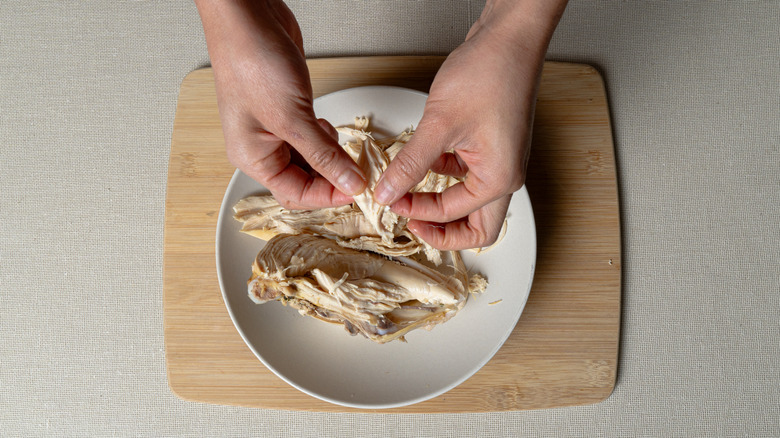 Hands shredding chunks of cooked chicken