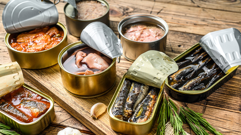 Various types of canned fish on a wooden board and counter