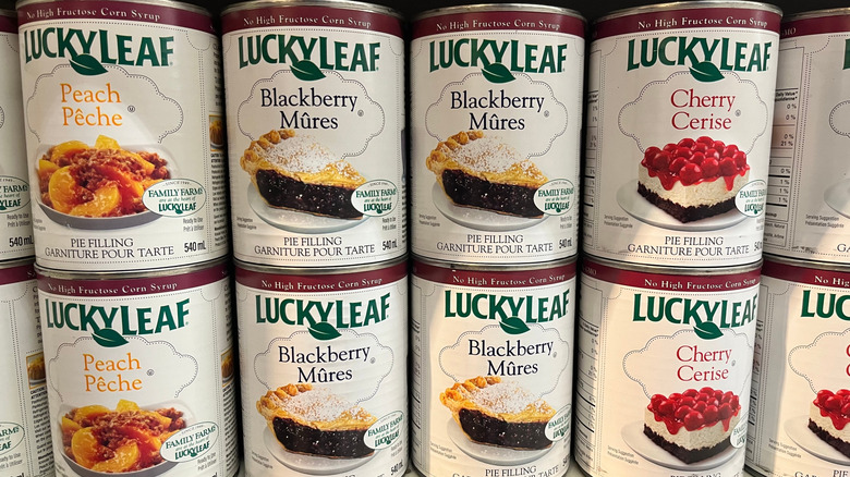 cans of different fruit pie fillings sit stacked on a grocery store shelf