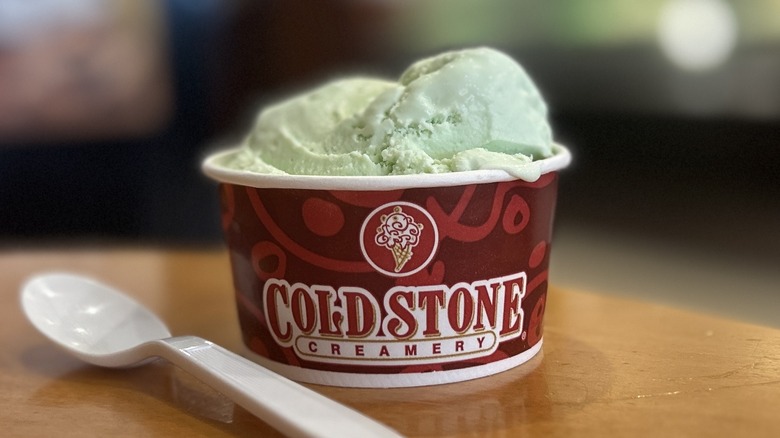 Cold Stone Mint Ice Cream in a small cup on a wooden table with a white spoon placed to the right of it