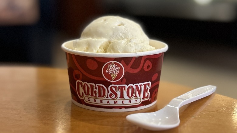 Cold Stone Sweet Cream Ice Cream in a small cup on a wooden table with a white spoon placed to the right of it