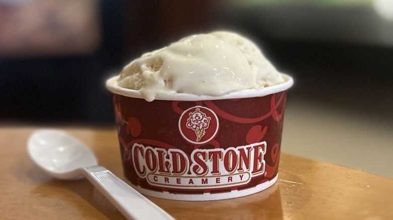 Cold Stone Cookie Dough Ice Cream in a small cup on a wooden table with a white spoon to the left of it