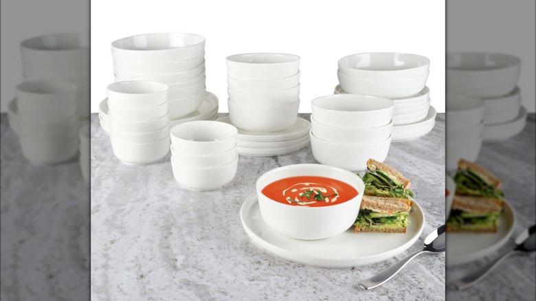 A Mikasa Samantha 40-piece Bone China Dinnerware Set sits on a stone surface, with a plated meal of a sandwich and tomato soup set out on dishes.