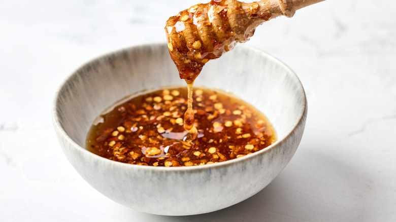 A honey spoon full of chile honey in a white bowl.