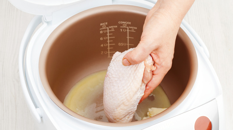 A hand putting chicken thighs into a slow cooker.