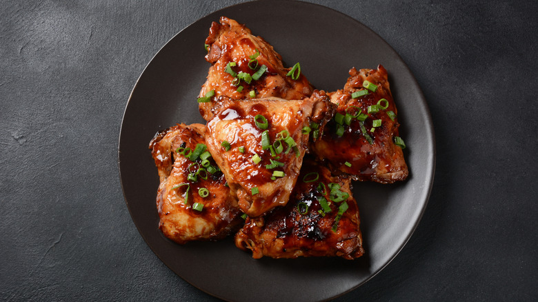 Chicken thighs on a black plate covered in green onions.
