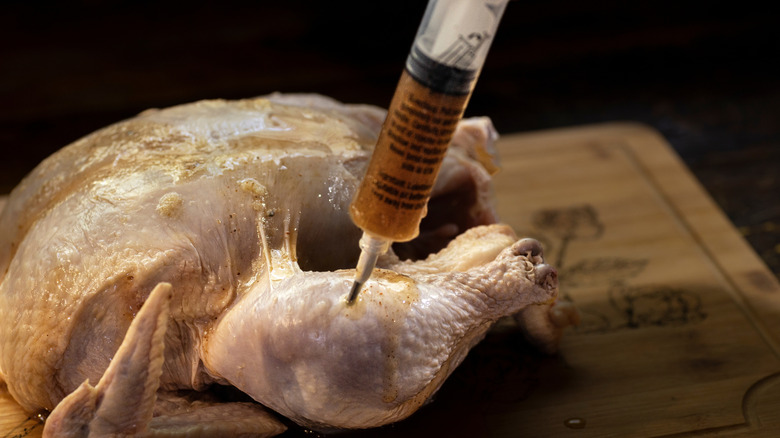 A person injecting chicken with a marinade.