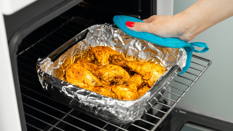A woman's hand removing a foil-lined baking dish filled with oven-baked fried chicken.