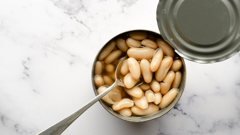 A can of cannellini beans with a spoon in them on a white marble surface