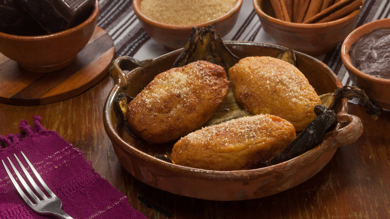 Three rellenitos de platano on plantain leaves on a rustic dish