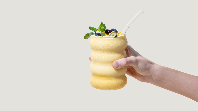 A hand holding a tropical smoothie with a white background