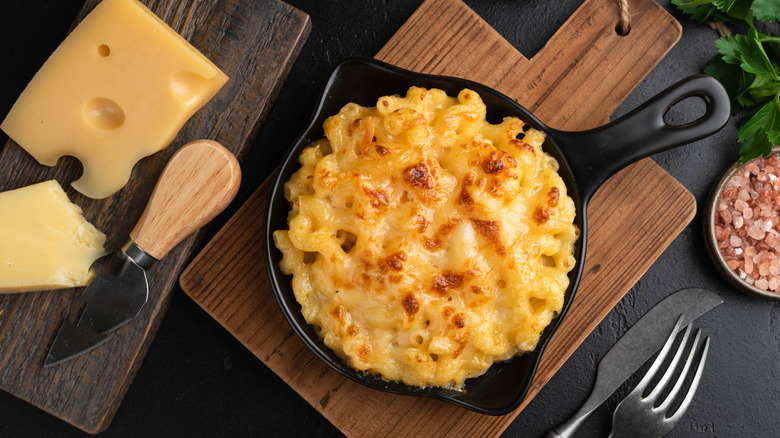 A delicious mac and cheese in a cast iron pan, with cheese and pick rock salt beside it