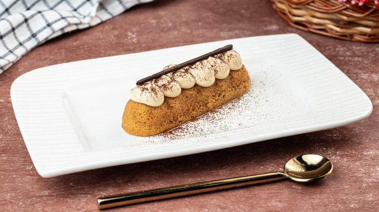 Éclair au café on a white plate with a golden spoon