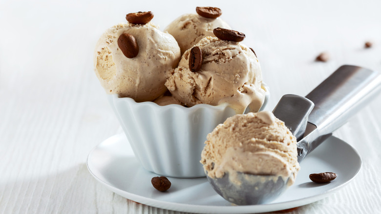 A scoop and white ceramic bowl full of coffee ice cream