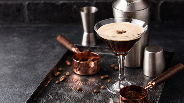 An espresso martini with bar tools and espresso beans