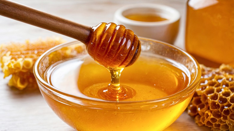 Honey dipper dripping above bowl of honey