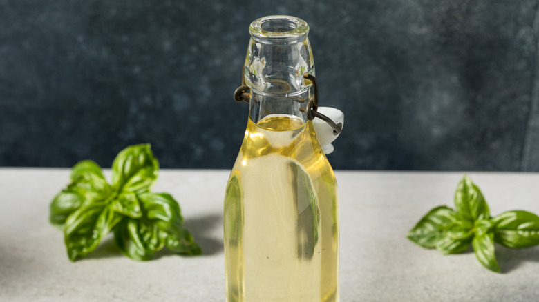 A glass bottle of clear simple syrup sits on a tabletop surrounded by basil sprigs