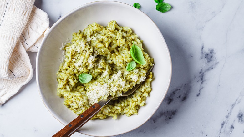 White bowl of pesto risotto with a fork, Parmesan, and fresh basil leaves