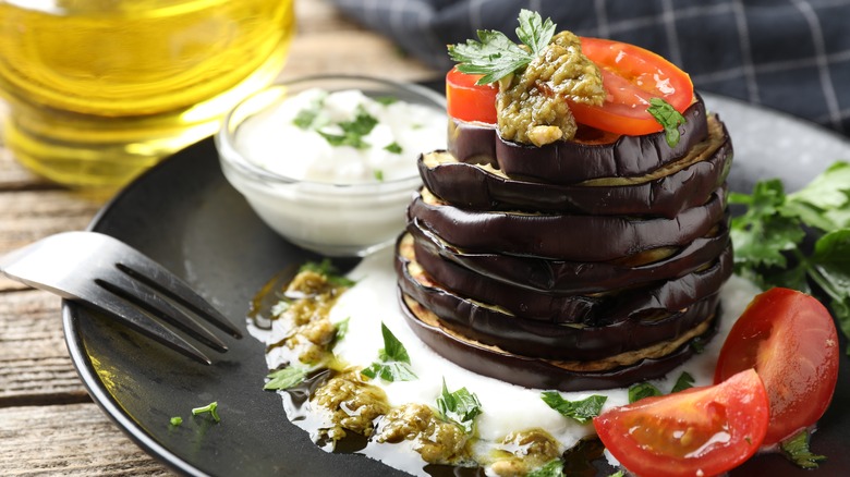 A stack of grilled eggplant rounds with pesto and fresh tomatoes