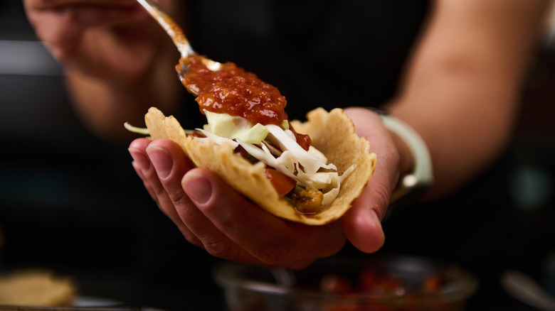 A woman spoons salsa onto a street taco in her other hand
