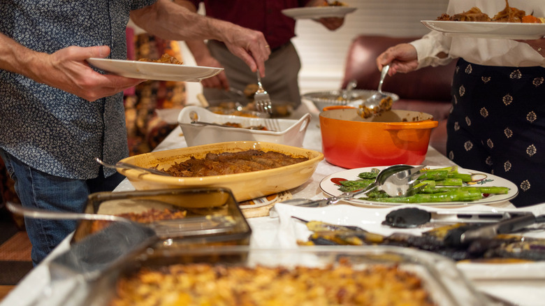 Guests fill plates with food from various dishes at a potluck dinner