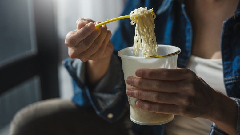 A woman eats instant noodles from a plastic cup