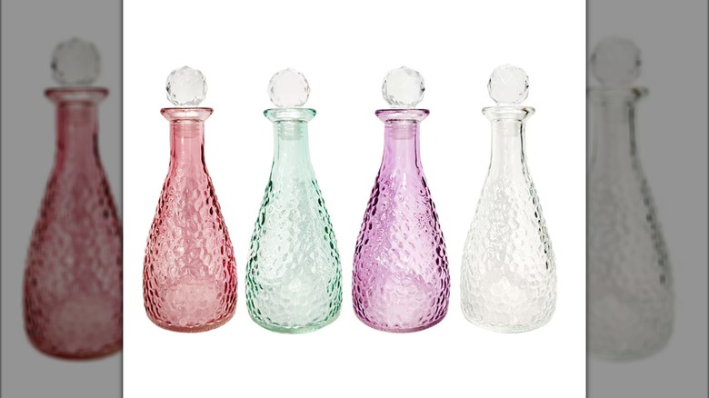 Four decorative glass bottles in burgundy, green, purple, and clear, with round crystal stoppers in their tops