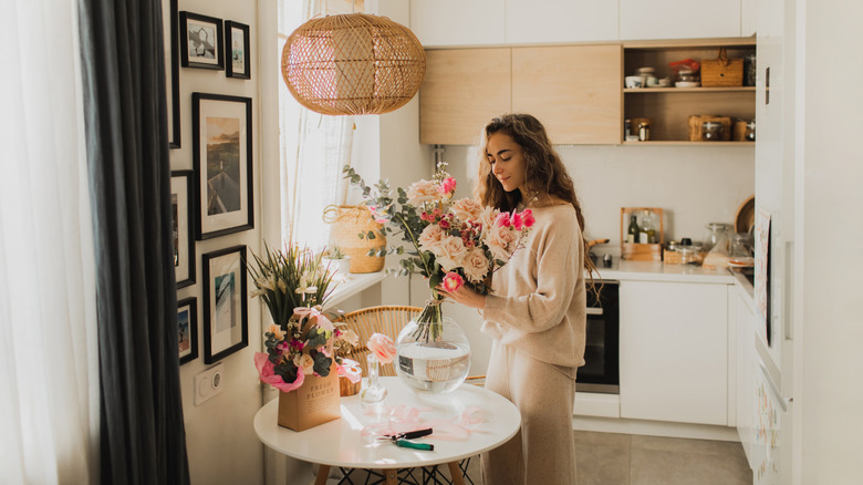A young woman arranges flowers on a small, round, white table in a kitchen