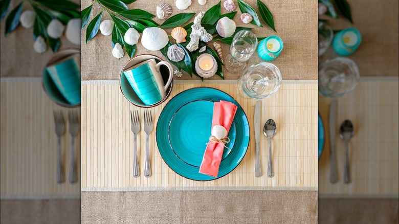 Turquoise dinnerware set on a bamboo placemat, surrounded by seashells and other beach decor