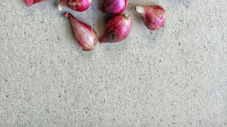 A head of unpeeled garlic with red shallots surrounding it