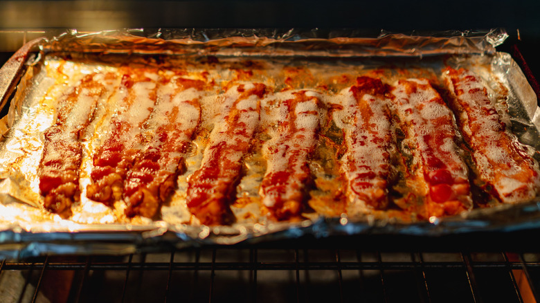 Bacon strips with foaming oil on a foil-lined baking sheet in an oven