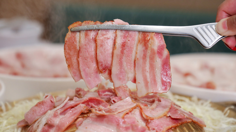 A person flips strips of bacon with small silver tongs